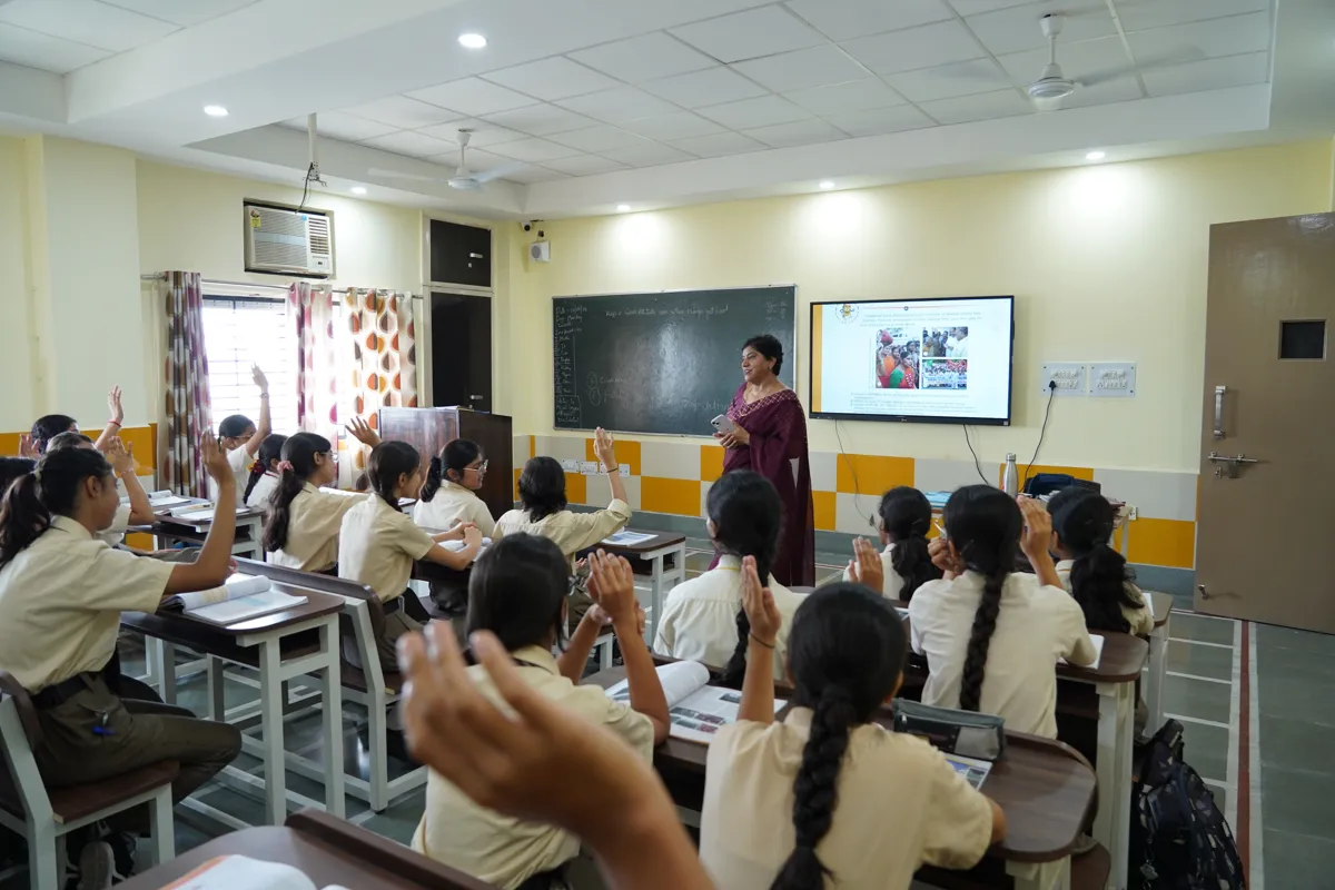 Teacher at the smart board while students raise their hands in a class at SKS World School, Greater Noida West