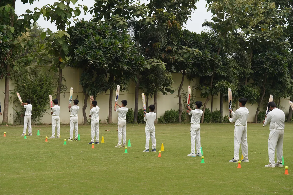 Students in cricket whites practising batting on the school ground, SKS World School, Greater Noida West